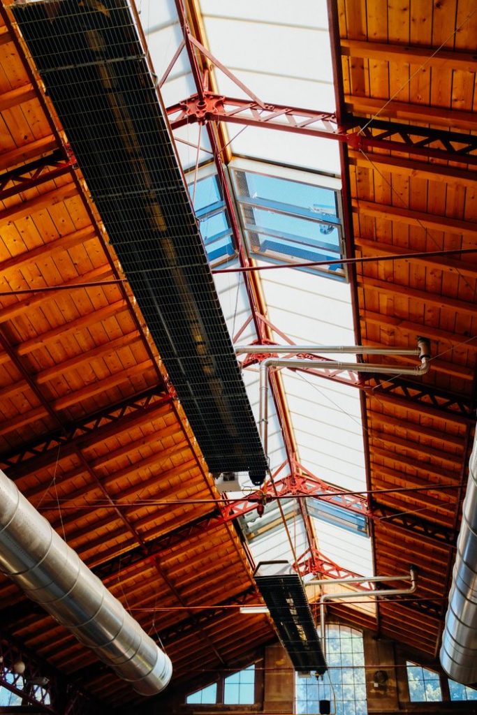 From below of long ceiling with glass and wooden details and iron pipe in daytime