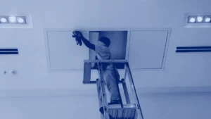 Técnico en una escalera revisando el falso techo por un panel de acceso
